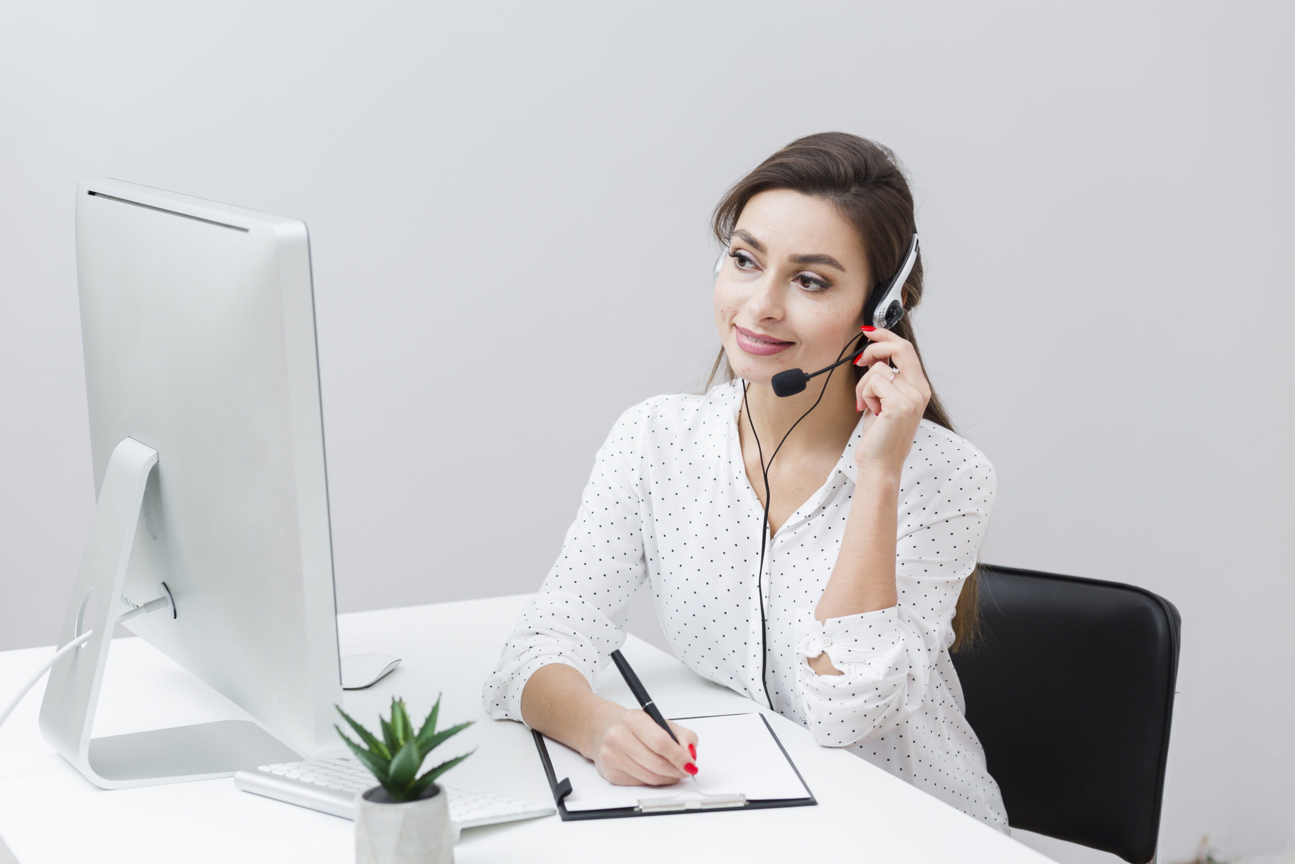 front view smiley woman writing something down while talking headset